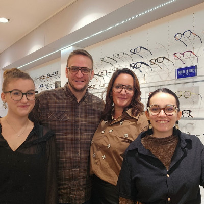 Équipe de quatre opticiens dans leur magasin d’optique à Namur, devant une présentation de montures de lunettes.